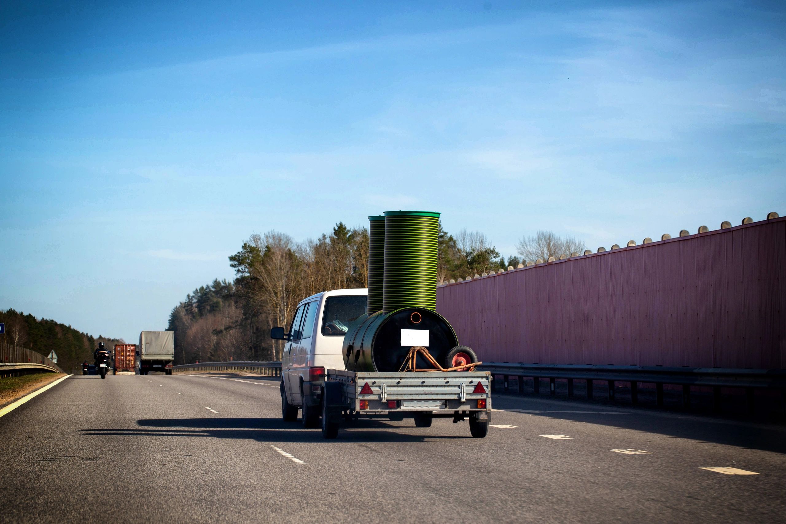 White van towing large pipes on a highway